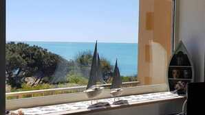 Een kamer met een groot raam met uitzicht op de kust, met een klein plankje met decoratieve objecten.