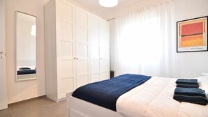 Een slaapkamer met een bed, een garderobe, een spiegel en een schilderij aan de muur.