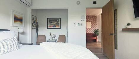 Habitación de hotel con una cama grande, un escritorio y una silla. Se ve una puerta que da a un baño y un pasillo.