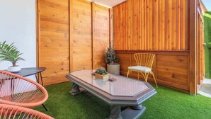 Een klein terras met een houten muur, een tafel, twee stoelen en een potplant.