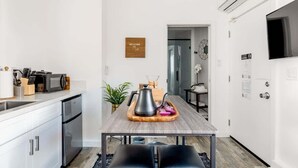 A modern kitchen with white cabinets, a wooden dining table, and a black kettle. - Bright Modern Stay | Near LAX & Stadiums I Patio (Los Angeles)