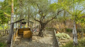 A wooden playhouse with a roof, surrounded by trees and a gravel path.