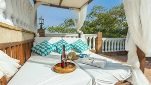 A bed with white linens, a bottle of wine, and a glass on a wooden tray.