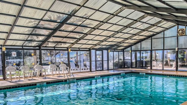 Ein Innenpool mit großen Glaswänden, einem Metalldach und einem Poolbereich mit Stühlen und einer Leiter.