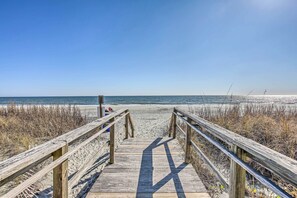 Walk along the beachside boardwalk, flanked by railings, to the sandy shore.