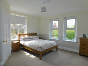 Quarto com cama de madeira, duas mesas de cabeceira, cômoda e duas janelas com vista para o verde.