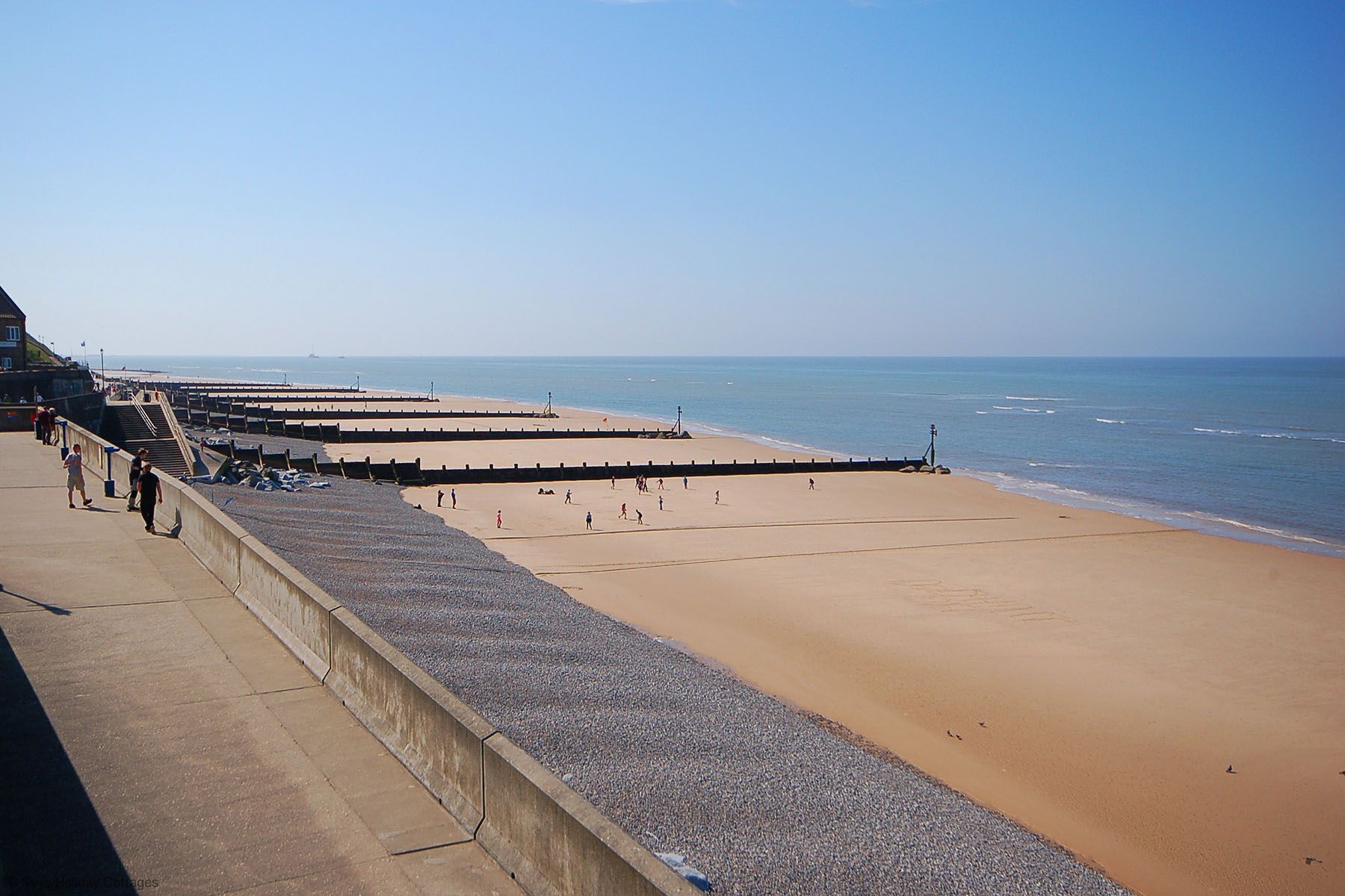 Uma praia com calçada de concreto e área de pedregulhos.