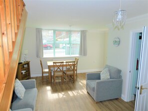 A living room with a dining table, two sofas, a chandelier, and a window with curtains. - Morris House -  a house that sleeps 11 guests  in 6 bedrooms (Sheringham)