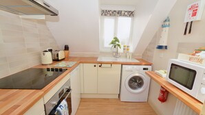 A compact kitchen with a washing machine, a microwave, and a toaster. - Gull View -  a second floor apartment that sleeps 4 guests  in 2 bedrooms (Sheringham)
