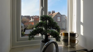 A window with a view of buildings and a bonsai tree on a windowsill. - Gull View -  a second floor apartment that sleeps 4 guests  in 2 bedrooms (Sheringham)