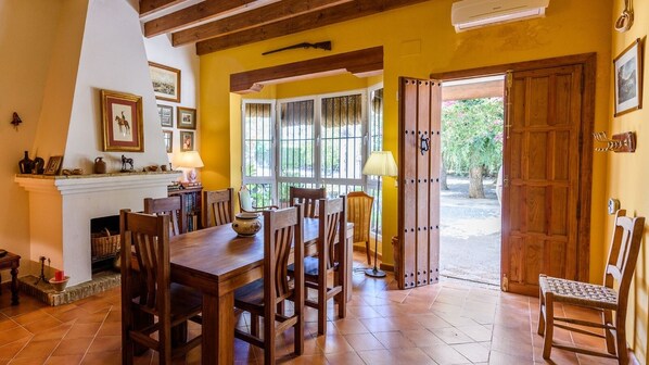A dining area with a wooden table and chairs, a fireplace, and a view of the outside. - Santa Ana de Marchena by Ruralidays (Seville)