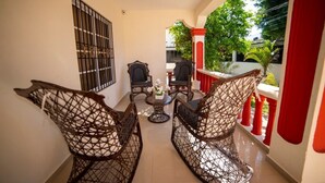 Un balcon avec des fauteuils en osier, une petite table et une vue sur la verdure et les bâtiments.