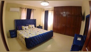 Cozy retreat with a large bed, tufted headboard, and patterned bedspread, accompanied by a wardrobe and bedside table with a lamp.