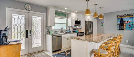 A modern kitchen with a central island, stainless steel appliances, and a dining area with wicker chairs.