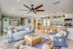 A spacious living area with a sofa, ottoman, wicker chairs, and a dining set.