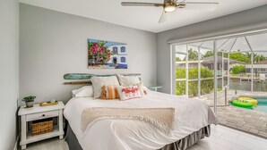 A bedroom with a bed, a nightstand, a ceiling fan, a window with a view of a pool, and a painting on the wall. - Canalfront Cape Coral Home with Dock & BBQ! (Cape Coral)