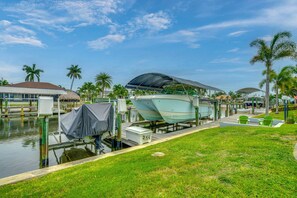 A marina with boats docked, a covered boat lift, and a grassy area with chairs.