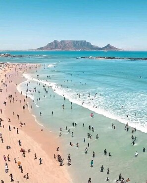 A beach with people swimming and walking along the shore, a clear sky, and mountains in the background. - ❄✨ Ocean front,  rooftop , gated single family beach house withsecurity guard❤️ (Limbe)
