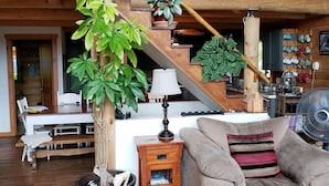 Ein gemütliches Wohnzimmer mit einer Holztreppe, einer großen Topfpflanze, einer Couch und einem gemusterten Teppich.