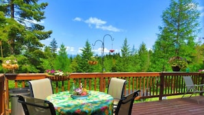 Eine Holzterrasse mit Tisch und Stühlen, umgeben von üppigem Grün und Bäumen.