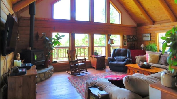 Ein gemütliches Blockhaus mit großem Kamin, Holzbalken und einem geräumigen Wohnbereich mit Sofa, Sesseln und Couchtisch.