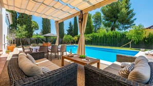 Ein Außenbereich mit Terrassenausstattung aus Rattan, einem Pool und einer Pergola, die Schatten spendet.