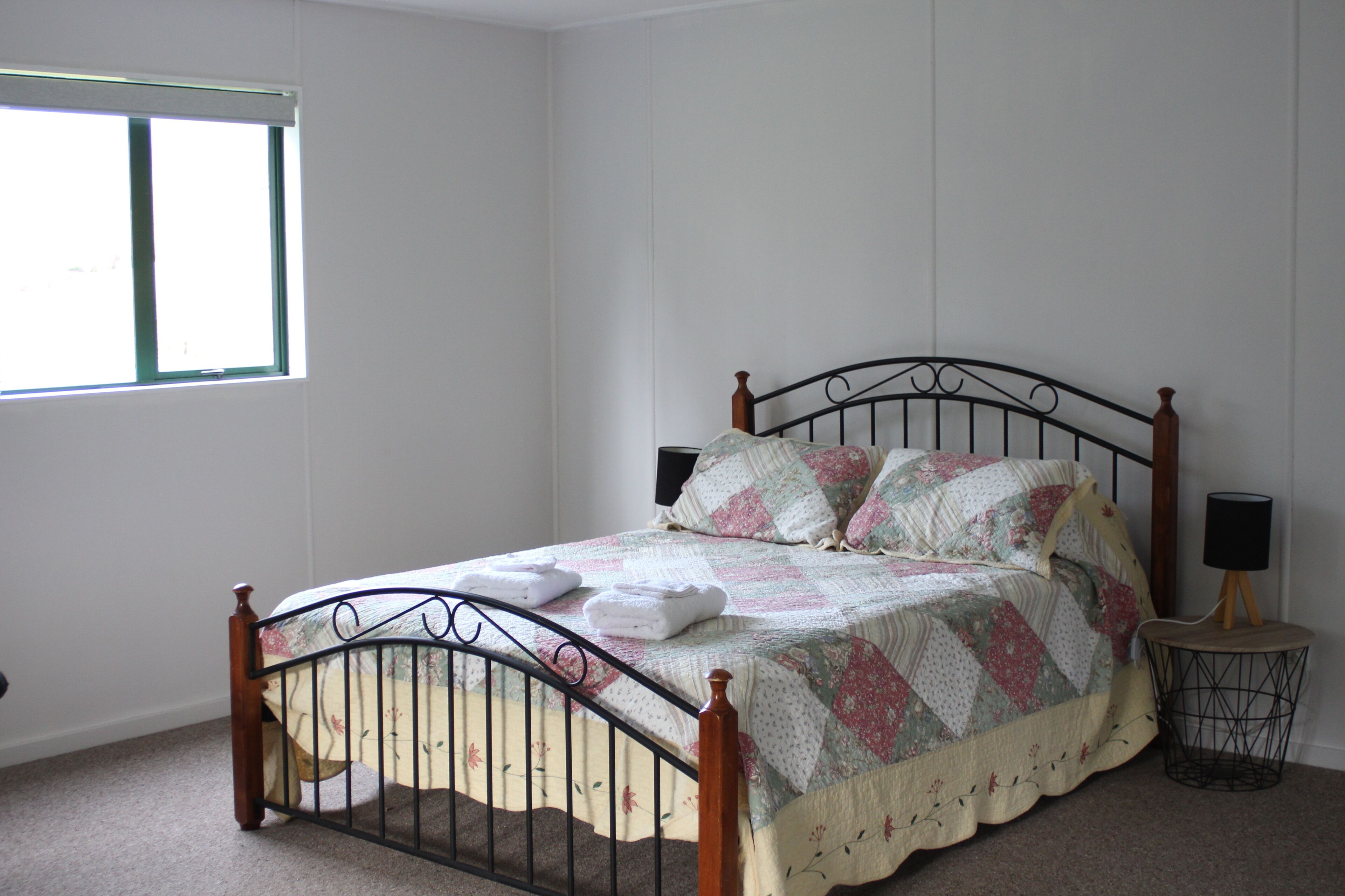 A bedroom with a bed, a window, and a bedside table with a lamp.