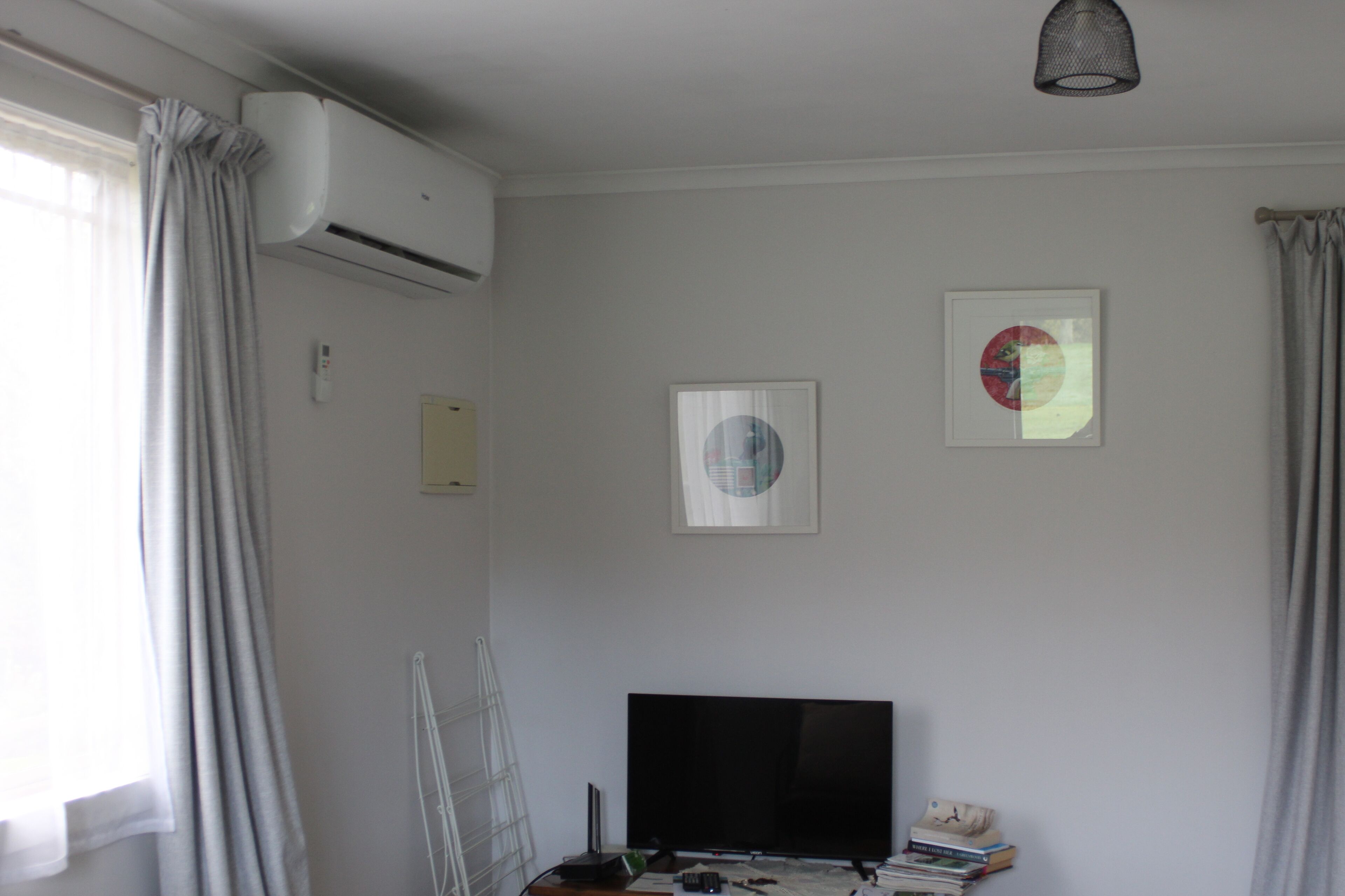 A room with a flat-screen TV, air conditioning unit, and two framed pictures on the wall.