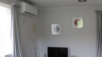 A room with a flat-screen TV, air conditioning unit, and two framed pictures on the wall.