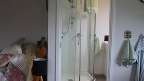 A bathroom with a glass-enclosed shower, a bed with a quilt, and towels hanging on the wall.