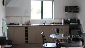 A compact kitchen with a gas stove, sink, and a microwave. There is a window above the sink, and a dining table with chairs.