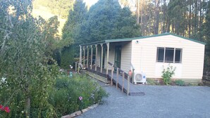 A small, single-story building with a porch and a gravel driveway, surrounded by dense greenery.