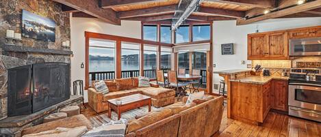Una sala de estar acogedora con chimenea, muebles de madera y grandes ventanales con vista a un lago.