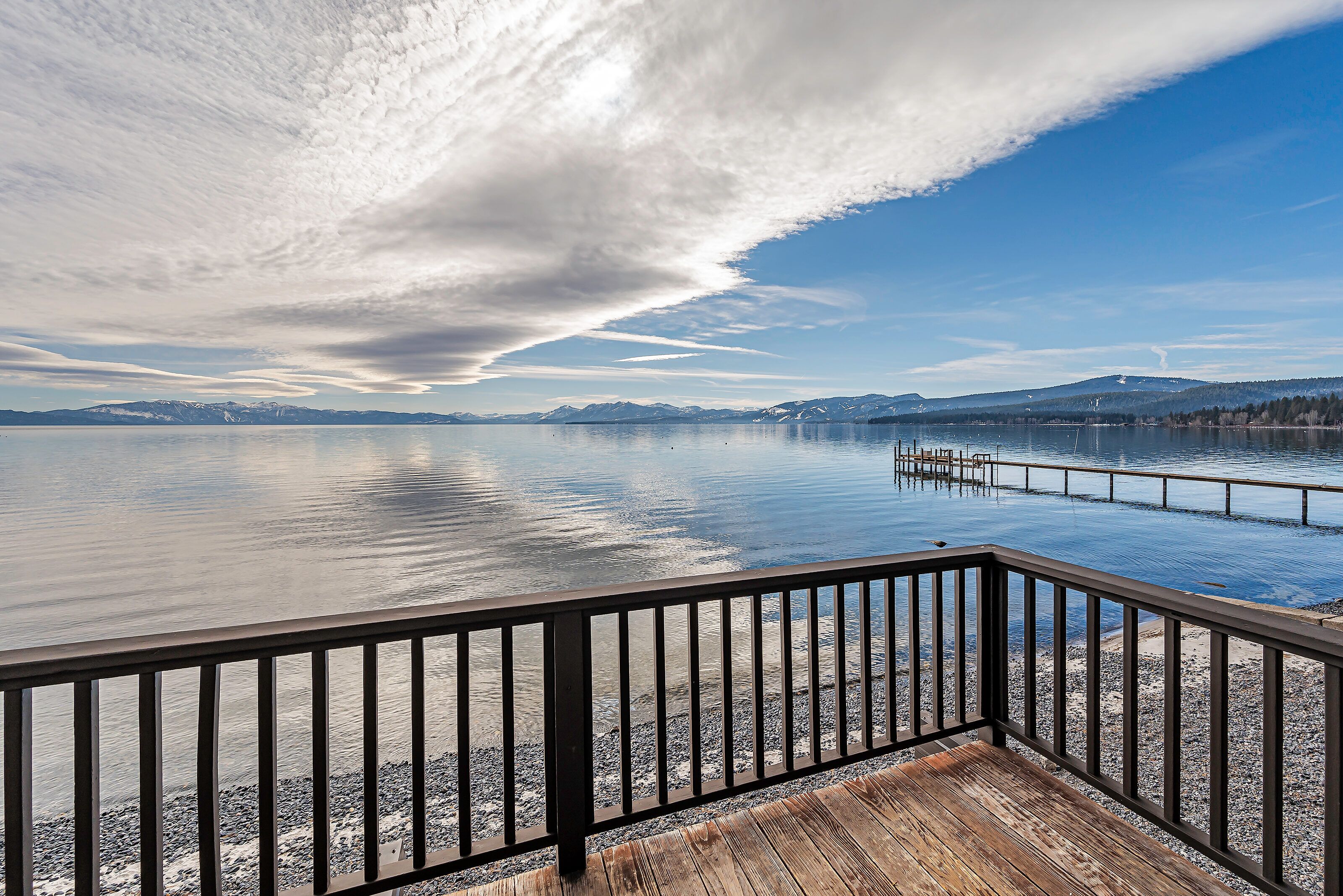 Une terrasse en bois avec une balustrade, donnant sur un lac paisible, avec des montagnes en arrière-plan.