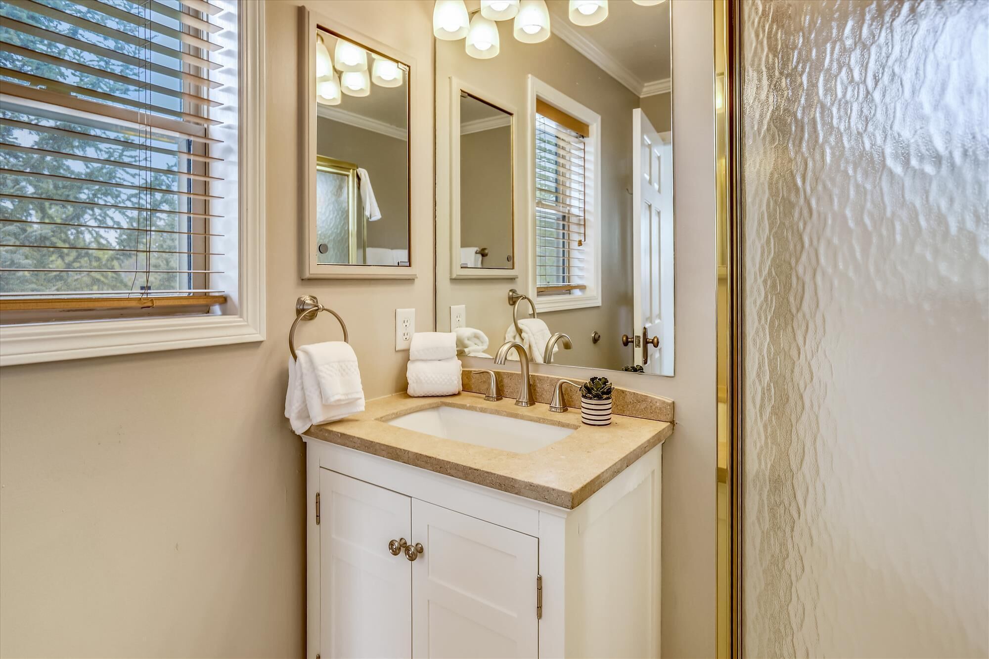 A bathroom with a sink, two mirrors, a towel rack, and a door with a textured surface.