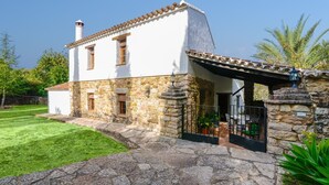 A two-story stone house with a white facade, a stone entrance, and a small patio area. - Ventorro del Herrero  Gaucín by Ruralidays (Málaga)