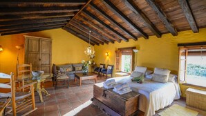 A cozy room with a bed, sofa, and dining table, featuring wooden beams and yellow walls. - Ventorro del Herrero  Gaucín by Ruralidays (Málaga)