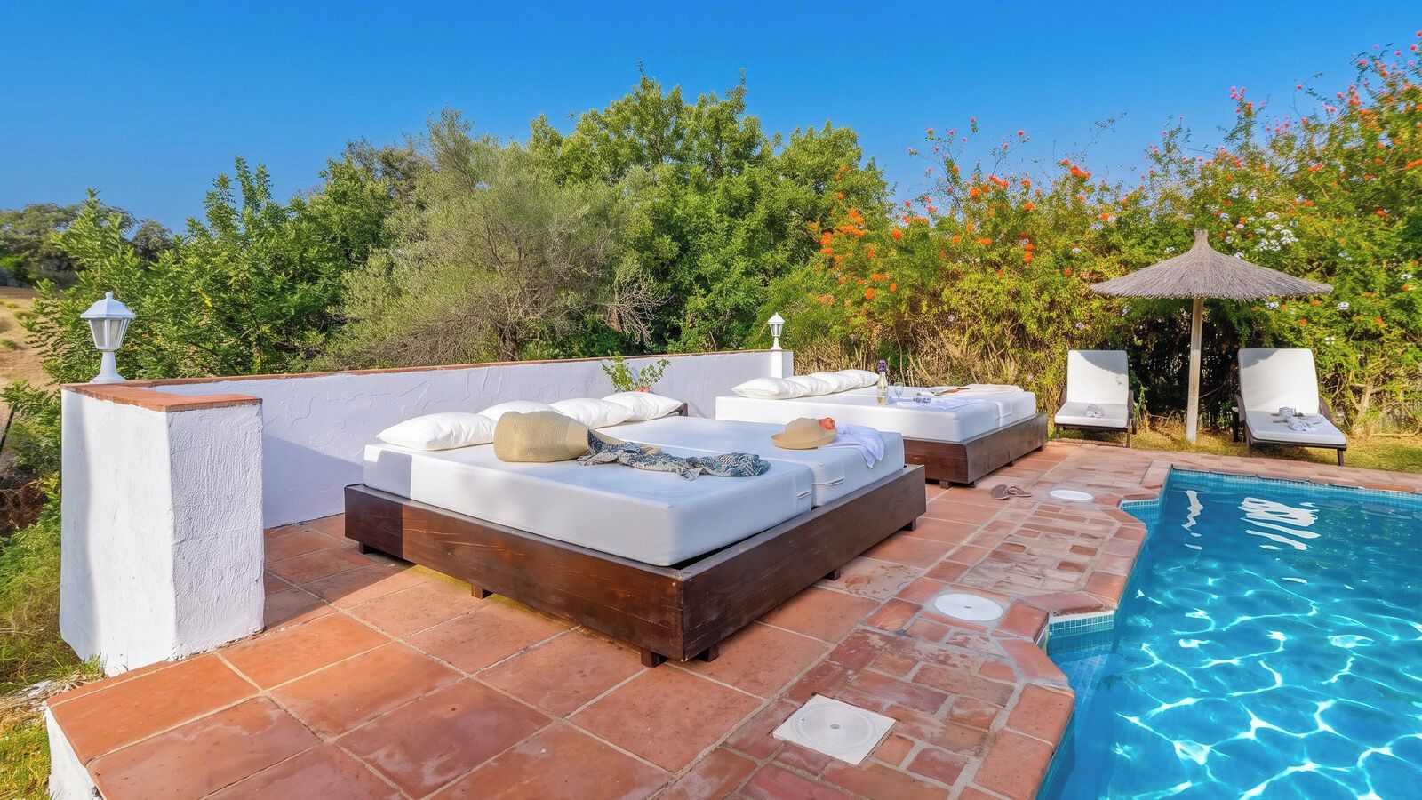 A poolside area with a wooden deck, white lounge chairs, and a small pool.