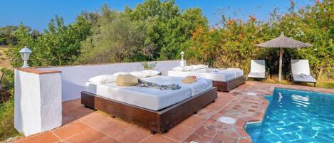A poolside area with a wooden deck, white lounge chairs, and a small pool.
