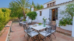 An outdoor patio with white tiled flooring, black metal chairs, and tables. There are potted plants and a white wall with a window. - Ventorro del Herrero  Gaucín by Ruralidays (Málaga)