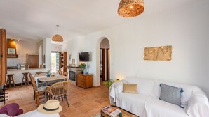 A spacious living area with a sofa, dining table, and chairs. There is a kitchen area with a TV and a fireplace.