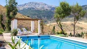A swimming pool with a view of mountains, a pergola, and lounge chairs.