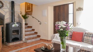 A living room with a stone fireplace, a staircase, a sofa with plaid cushions, and a vase of flowers. - Casa de la Abuela Gaucín by Ruralidays (Málaga)