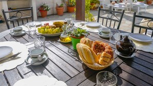 A round wooden table set for a meal with plates, cups, a basket of bread, a pitcher, and a bowl of fruit. - Casa de la Abuela Gaucín by Ruralidays (Málaga)
