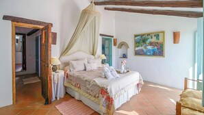 Une chambre à coucher avec un lit, des tables de chevet, un baldaquin, un tableau et une porte en bois rustique.