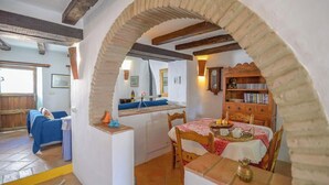Un coin repas accueillant avec une table dressée pour deux personnes, un espace cuisine avec un comptoir et des tabourets, et un espace de vie avec un canapé et une table basse.