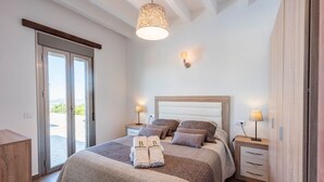 Une chambre à coucher comprenant un lit, deux tables de chevet avec des lampes, un luminaire au plafond et une porte-fenêtre coulissante donnant sur un espace extérieur.