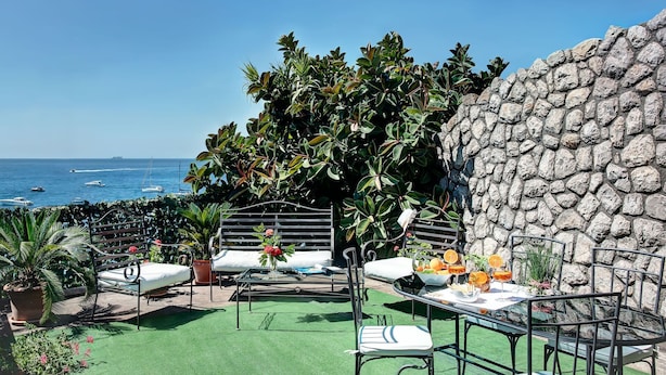 Une terrasse extérieure avec un mur en pierre, une pelouse artificielle verte et une vue sur la mer.