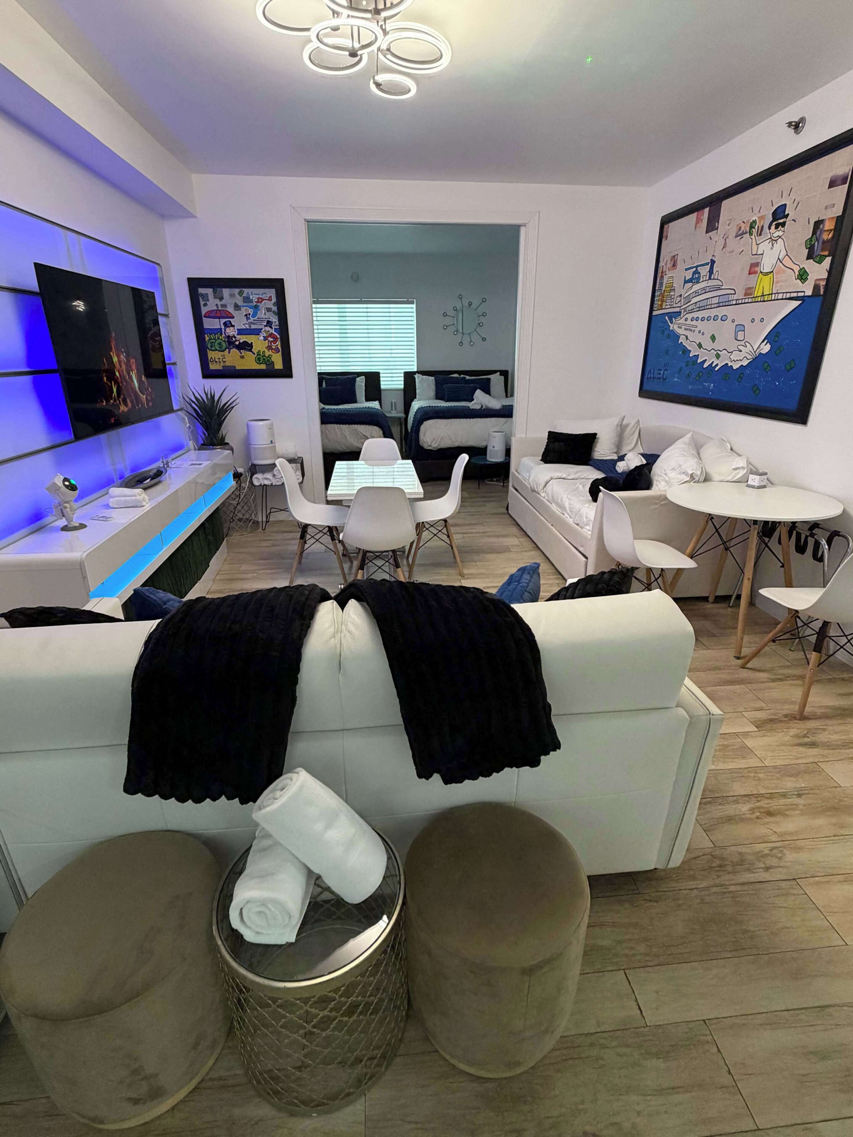 A modern living room with a sofa, dining table, and chairs, a TV, and artwork on the walls.