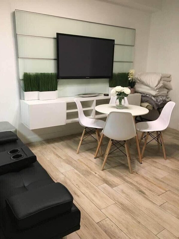 Ein modernes Wohnzimmer mit Flachbildfernseher, weißen Möbeln und Holzboden mit Fischgrätmuster.